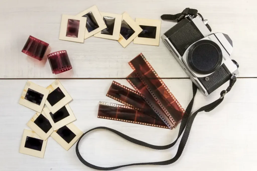 Film negatives, slides, and a vintage camera laid out on a table, used to illustrate Momento’s negative and slide scanning service.