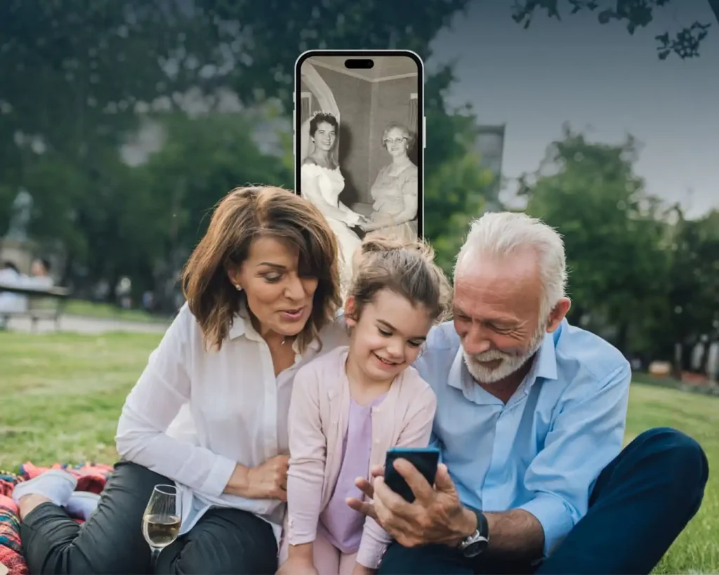 Grandparents and a child sitting together outdoors, viewing digitised family photos on a smartphone.Sharing family memories across generations, made possible through photo digitisation.