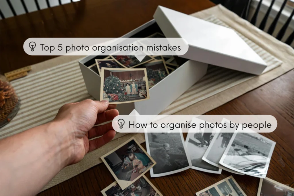 Hand organising old printed photographs from a storage box on a table, showing safe photo organisation tips